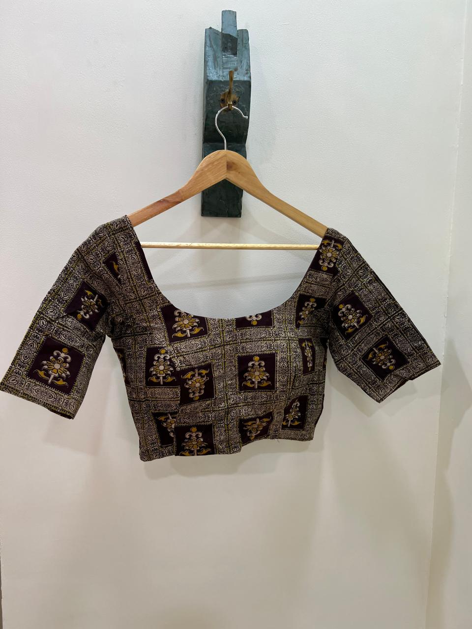 Black and gold patterned blouse on a hanger against a white wall