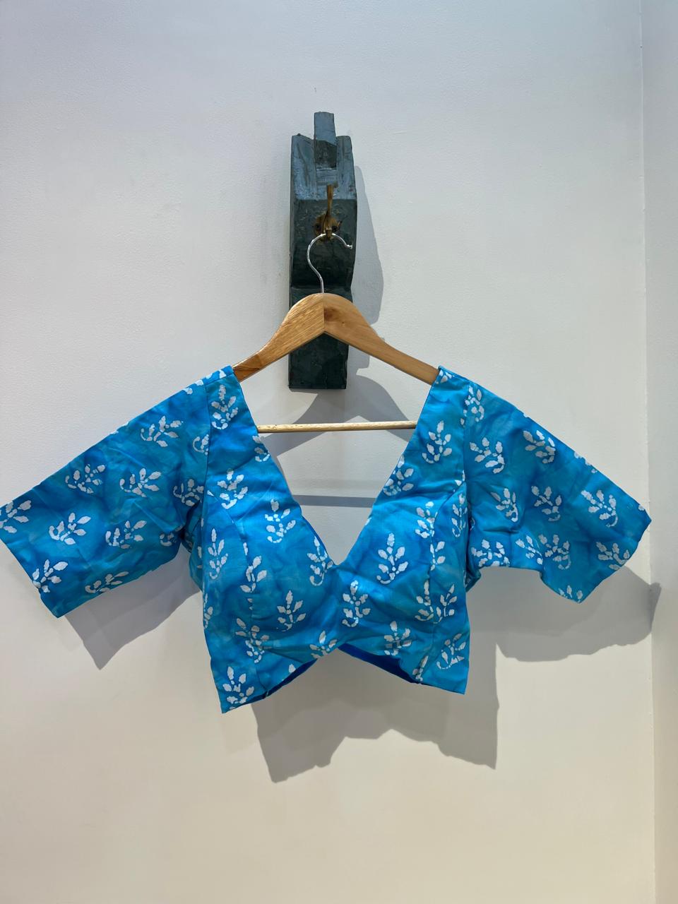 Blue patterned top on a wooden hanger against a white background