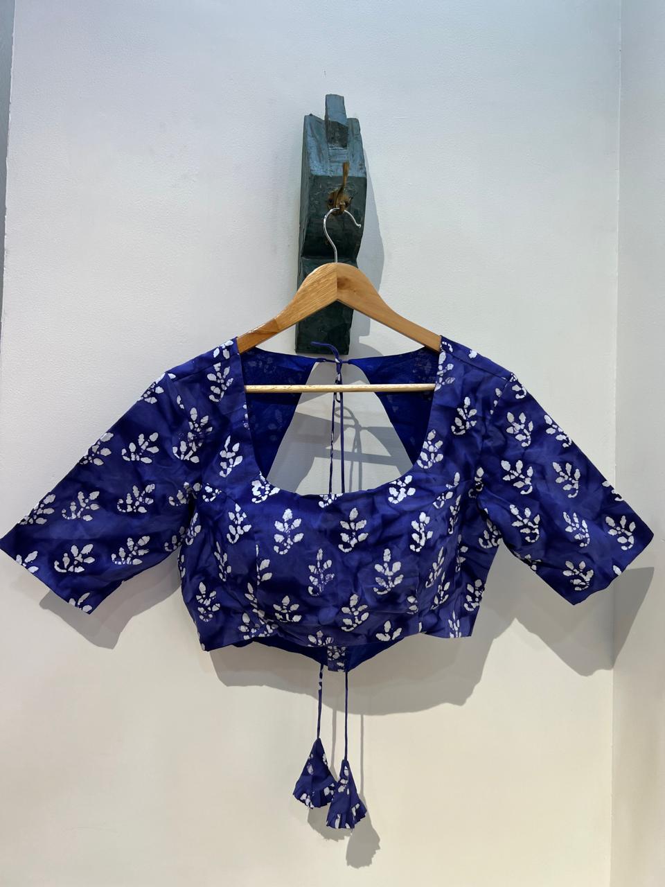 Blue blouse with white floral pattern on a hanger against a white wall