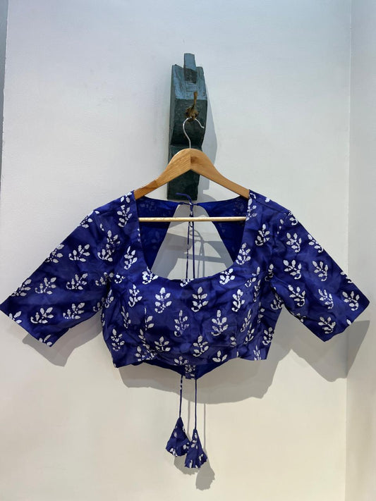 Blue blouse with white floral pattern on a hanger against a white wall