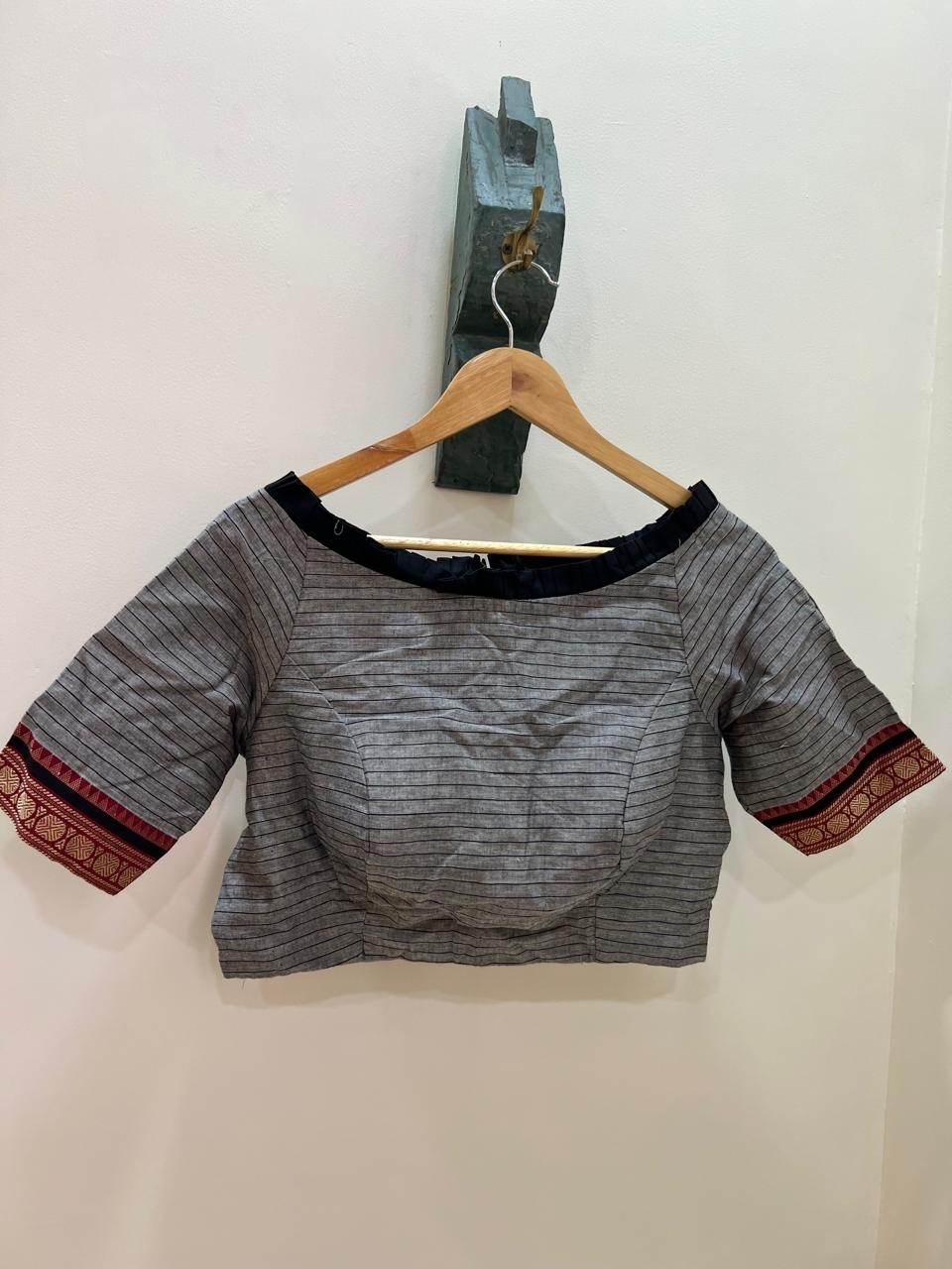 Gray blouse with red and black accents on a wooden hanger against a white wall.