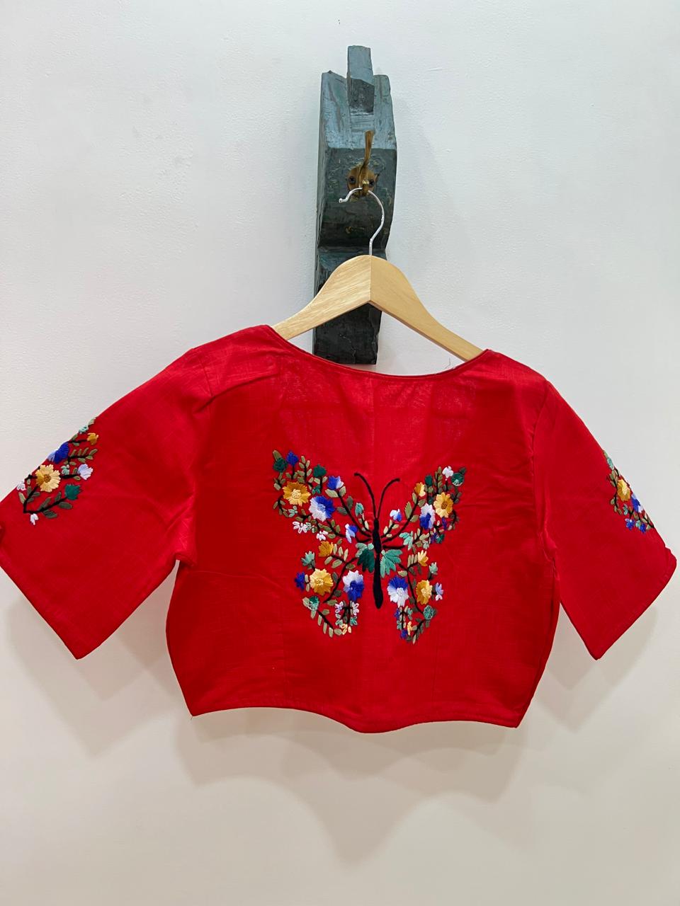 Red blouse with butterfly design on a hanger against a white background