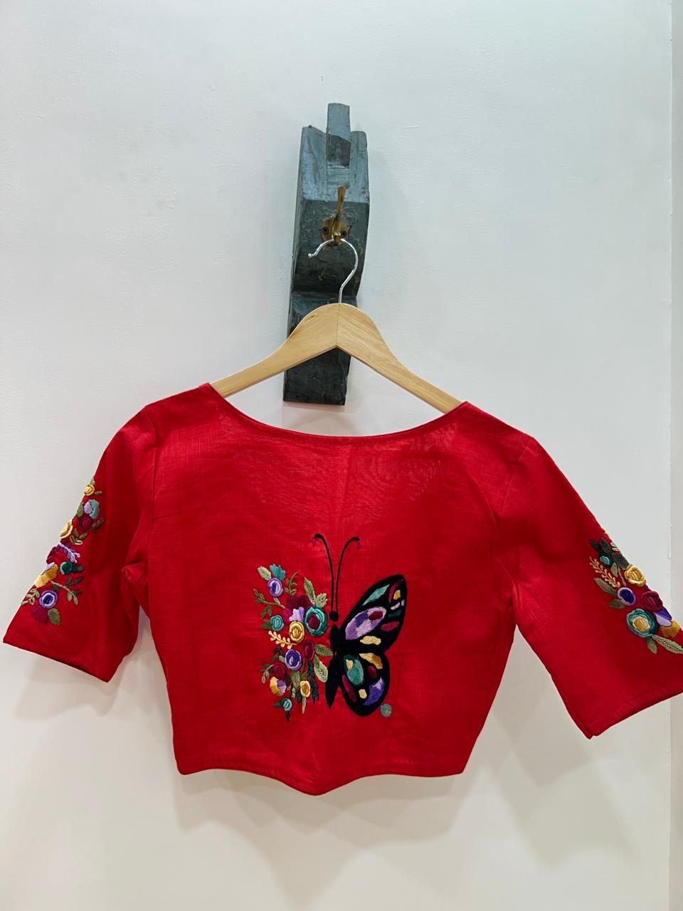 Red blouse with butterfly and floral embroidery on a wooden hanger against a white background